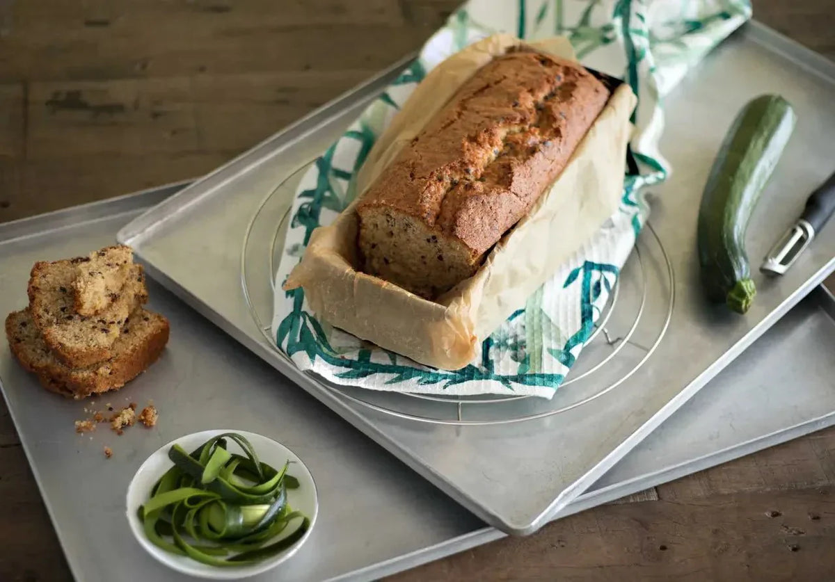 Zucchini-Kuchen in einer Brotform auf einem Blech mit Zucchinischeiben und einem frischen Zucchino daneben.