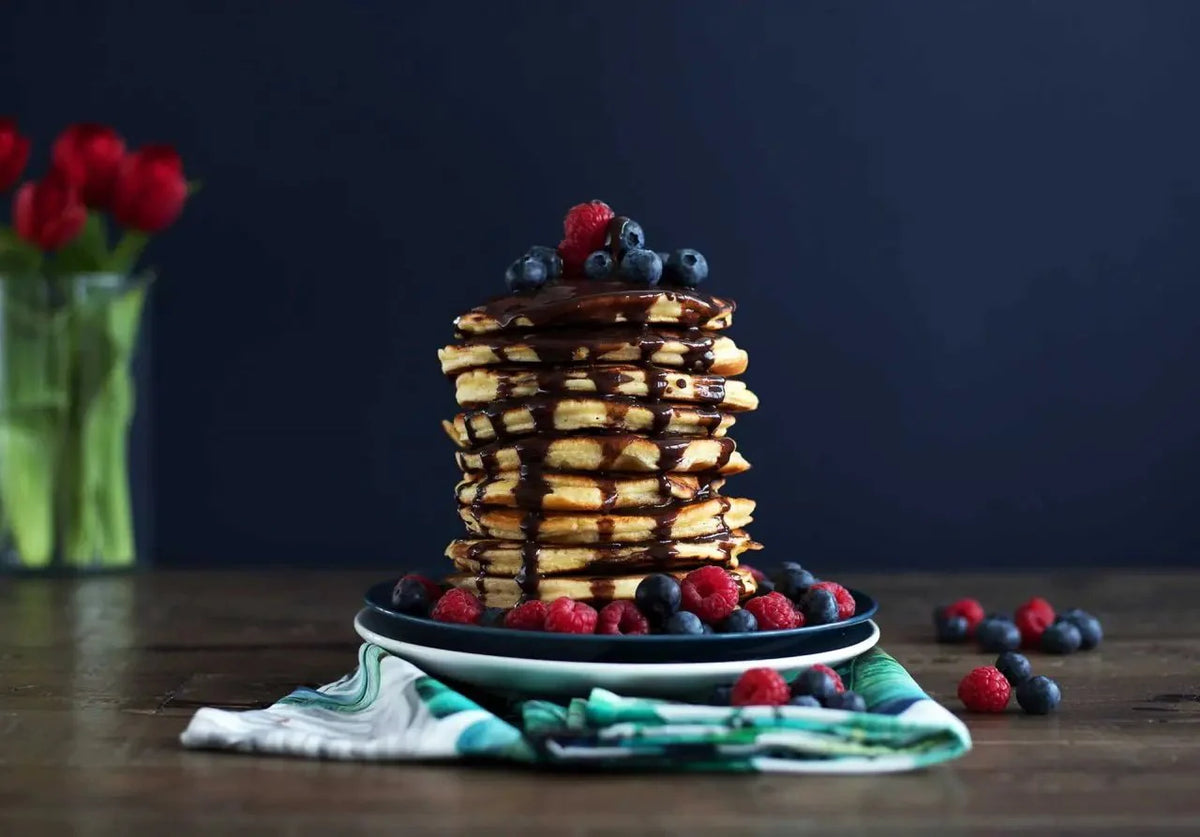 Stapel Fluffiger Pancakes mit Schokoladen-Ahornsirup und Beeren, serviert auf einem Teller mit dunklem Hintergrund.