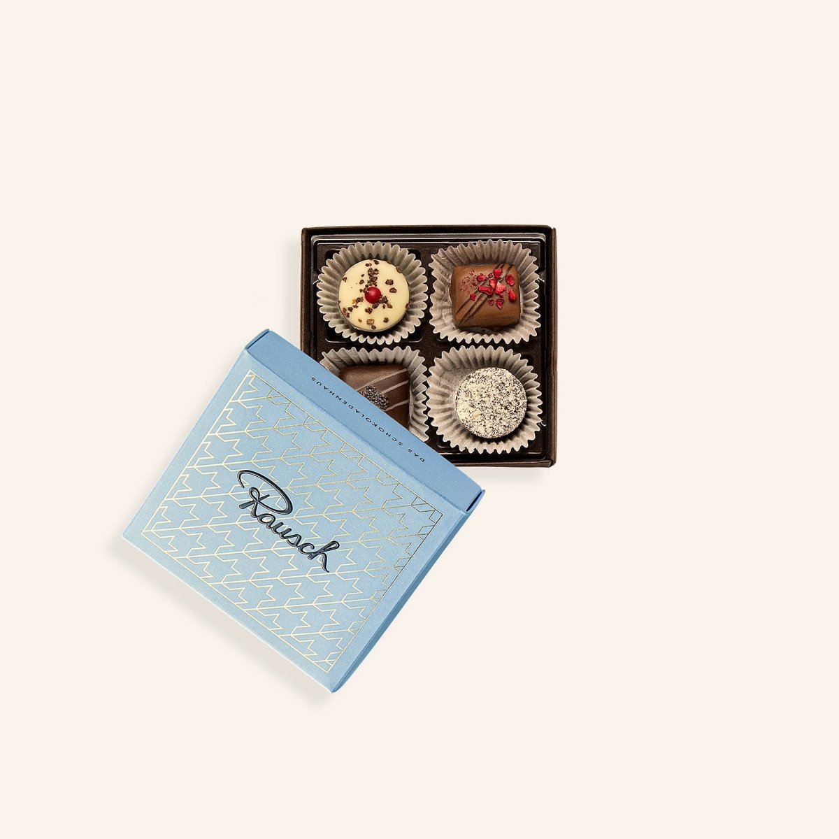Offene Schachtel mit vier handgemachten Pralinen, hellblauer Deckel mit Rausch-Logo.