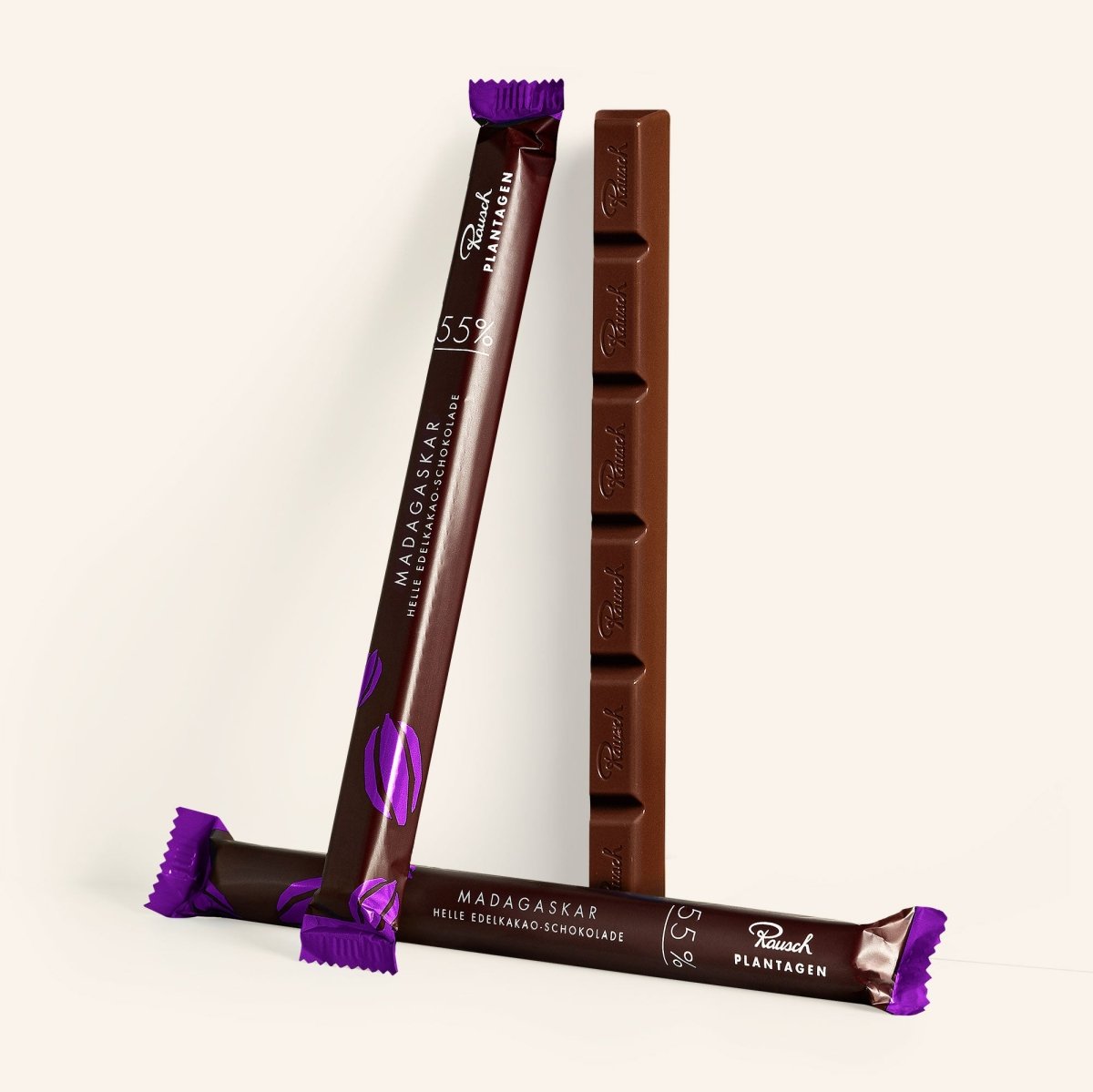 Drei Madagaskar 55% Schokoladensticks mit violettem Schriftzug, zwei stehend, einer liegend auf hellem Hintergrund.