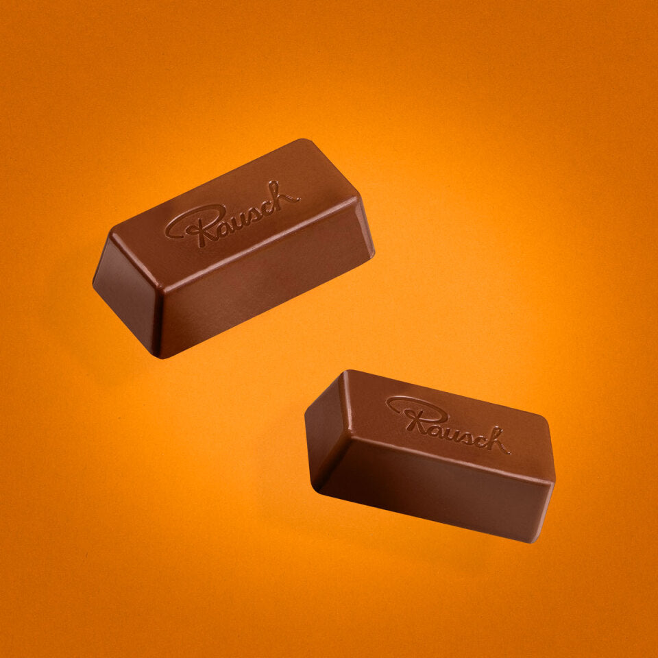 Zwei Schokoladen Minis von Rausch vor orangefarbenem Hintergrund, geprägt mit dem Rausch-Logo.