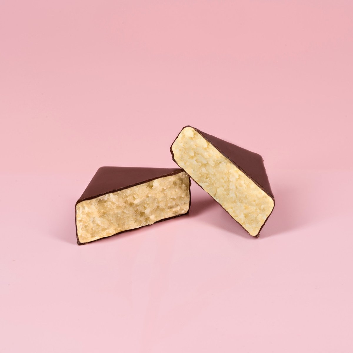 Halbes Schokoladen-Marzipan-Häppchen, schokoladeüberzogen, mit hellem Marzipan gefüllt, vor rosa Hintergrund.