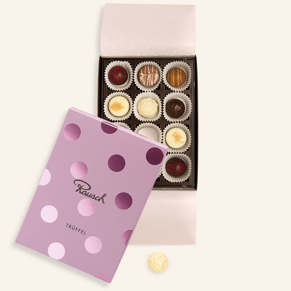 Geöffnete Pralinenschachtel mit 12 Trüffeln und pink gepunktetem Deckel, eine Praline liegt daneben.