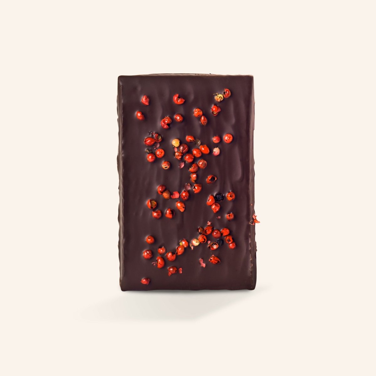 Dunkle Schokoladentafel mit rosa Pfefferkörnern, minimalistisch präsentiert auf hellem Hintergrund.