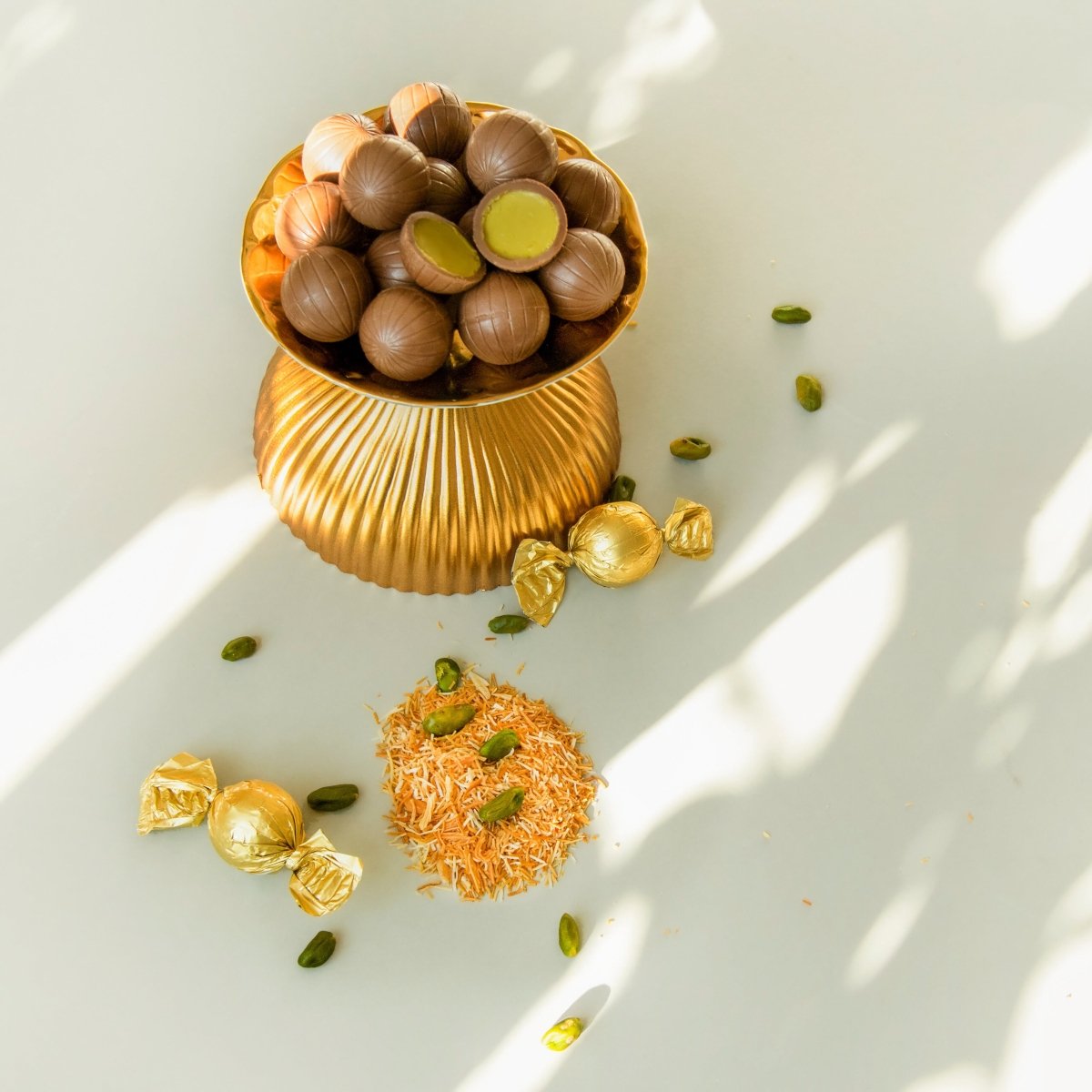 Elegante Schale mit Dubai Style Pralinenkugeln und Pistazien, auf hellem Hintergrund.