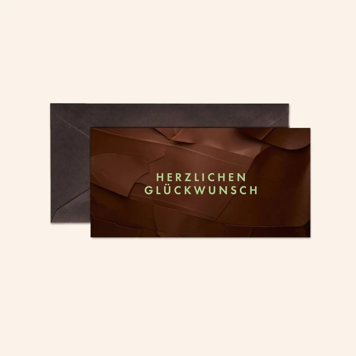 Braune Karte mit der Aufschrift "Herzlichen Glückwunsch" vor einem dunklen Umschlag.
