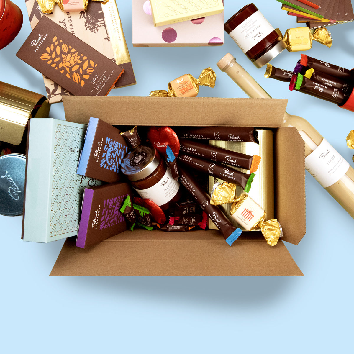 Offene Box mit verschiedenen Premium-Schokoladenprodukten von Rausch auf blauem Hintergrund.
