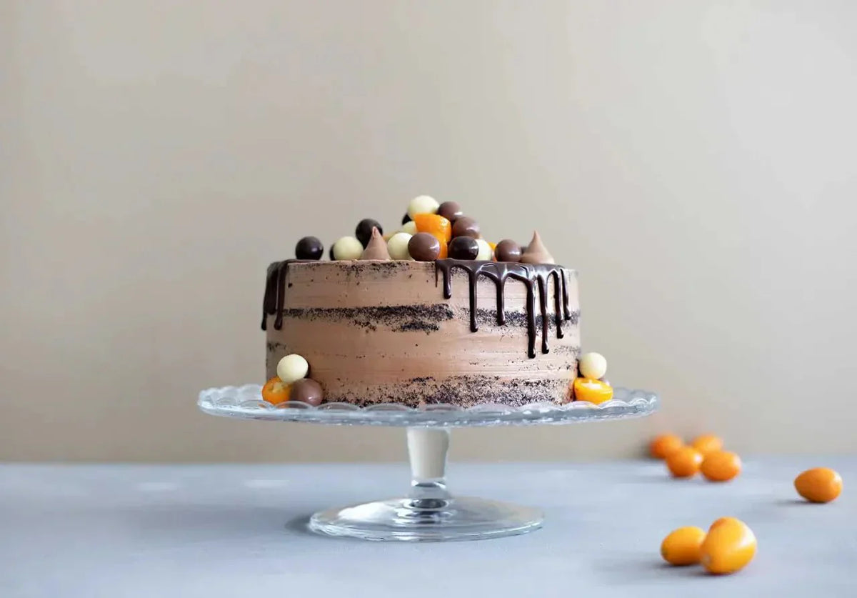 Naked Cake mit Edelako-Schokolade, Schokoglasur und bunten Schokokugeln auf Glasplatte.