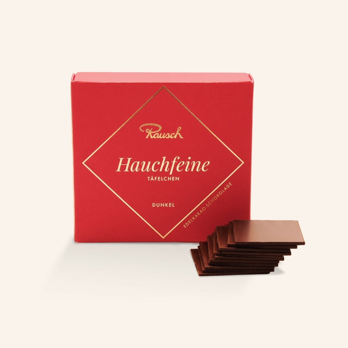 Rote Schachtel Rausch Hauchfeine Täfelchen, dunkel, mit gestapelten hauchfeinen Schokoladentafeln davor.