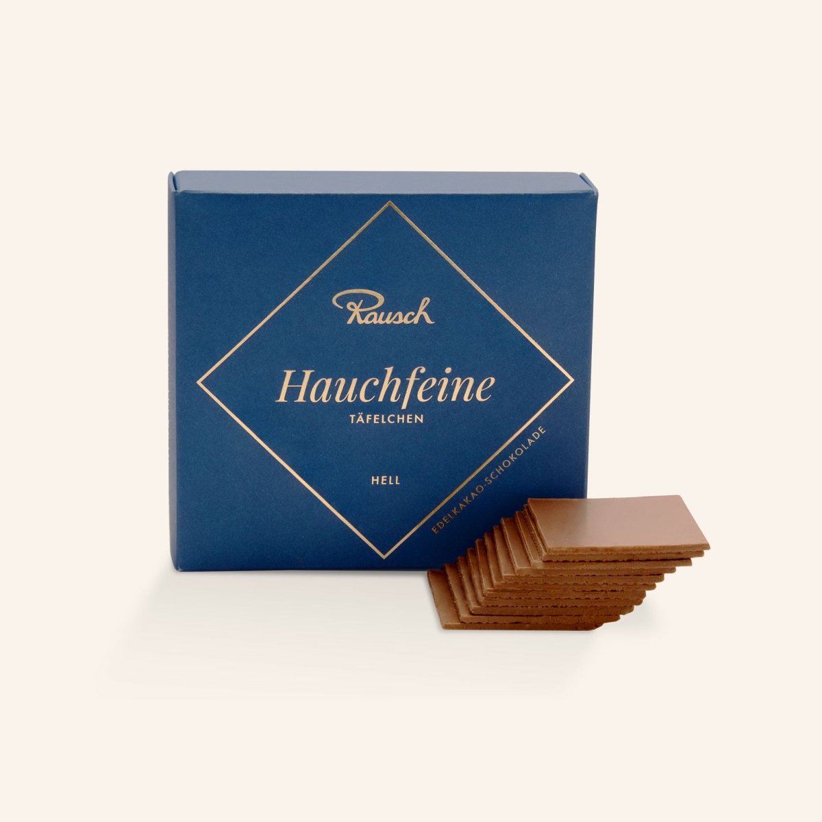 Blaue Rausch-Schachtel mit "Hauchfeine Täfelchen" in heller Schokolade, davor gestapelte Schokoladentäfelchen.