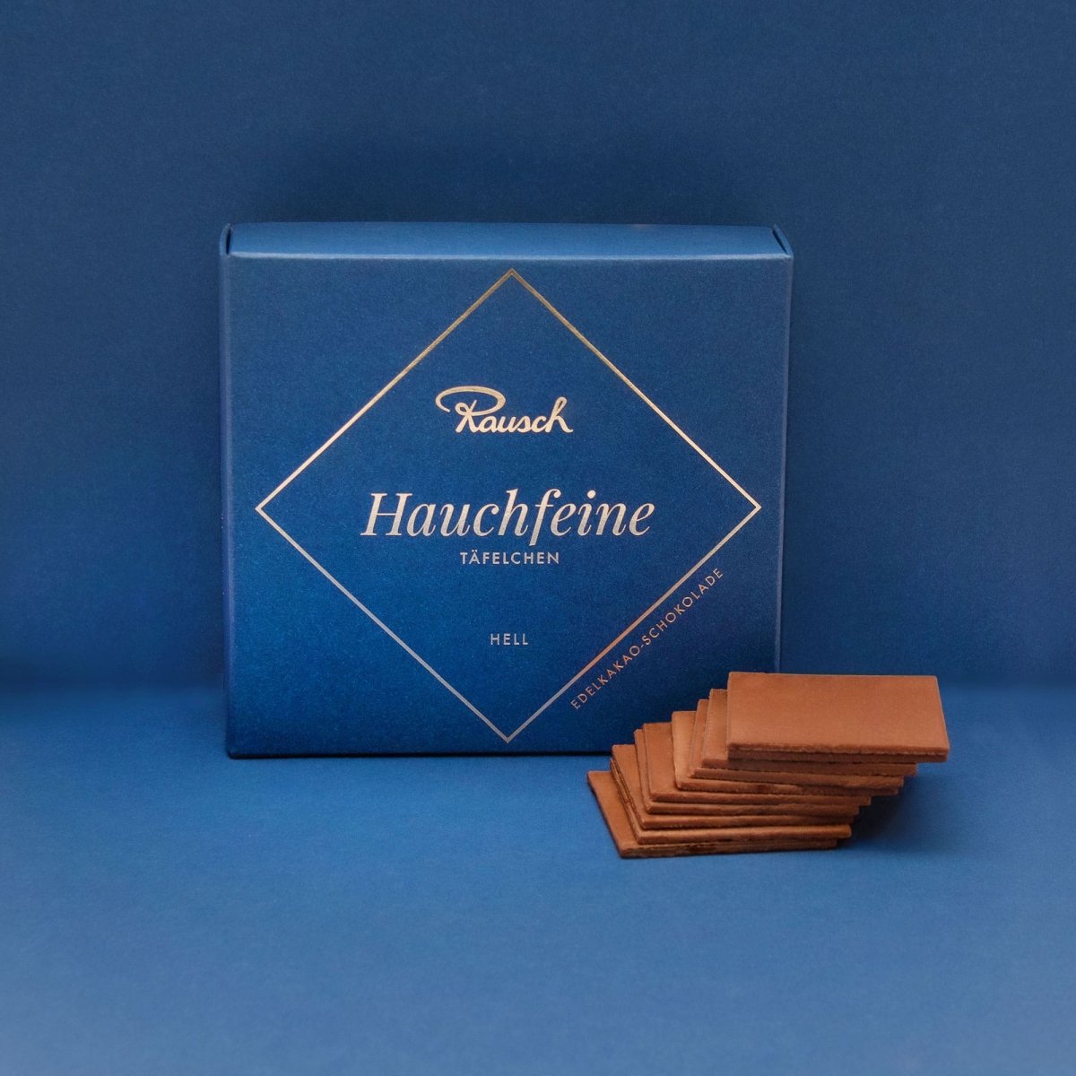 Edle Verpackung und dünne Schokoladentäfelchen auf blauem Hintergrund, Rausch Hauchfeine Hell-Schokolade.