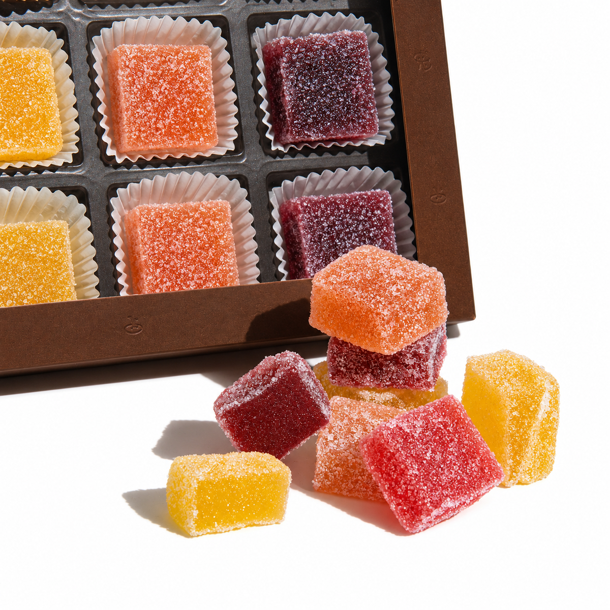 Bunte Fruchtgeleewürfel in verschiedenen Farben in und vor einer edlen Box angeordnet.
