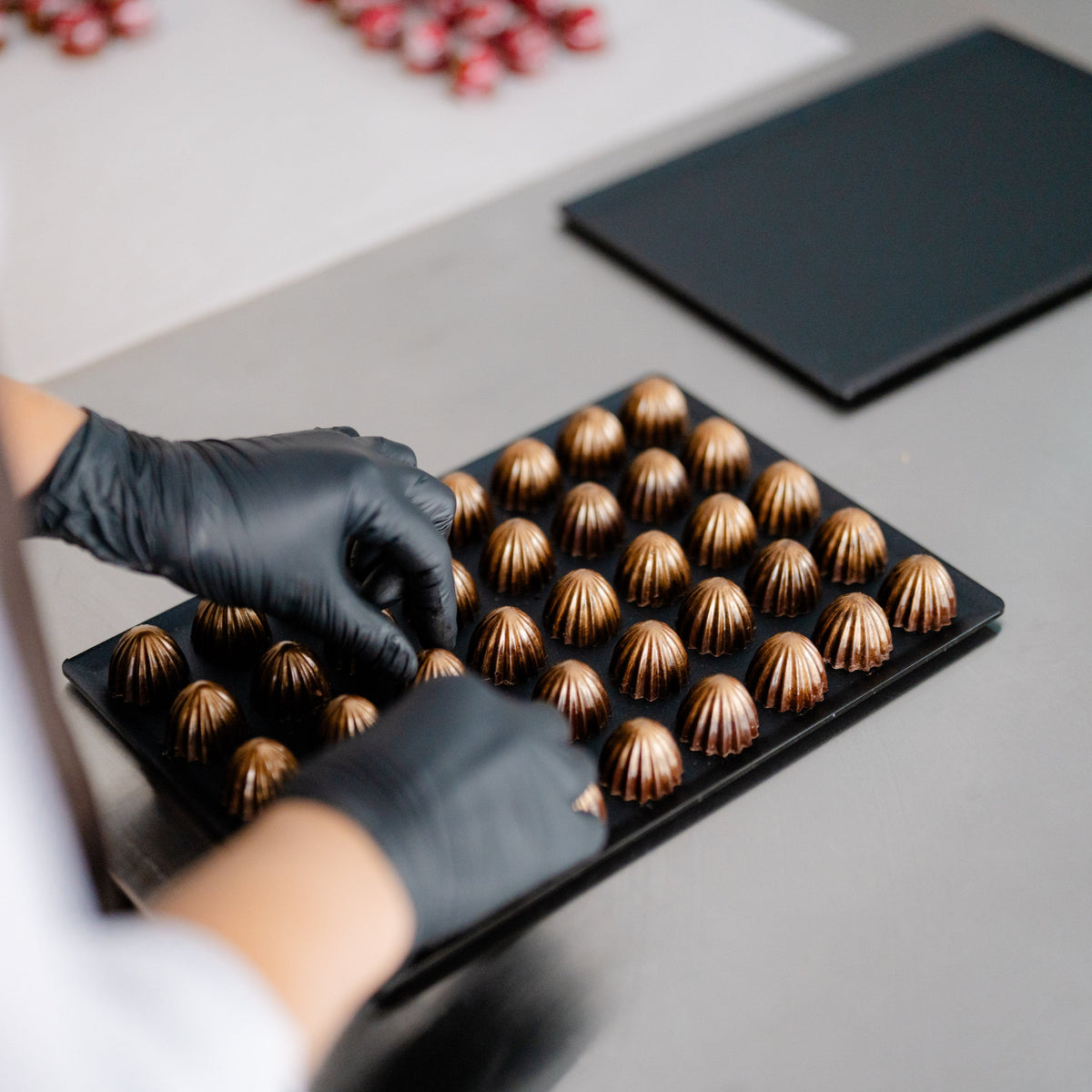 Person arrangiert handgefertigte Pralinen auf einem Tablett in einer Schokoladenmanufaktur.