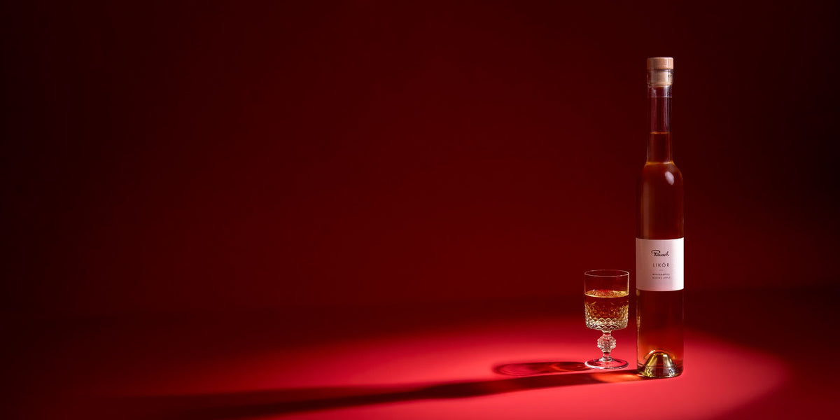 Eine Flasche Rausch Winterapfel-Likör mit Glas auf rotem Grund