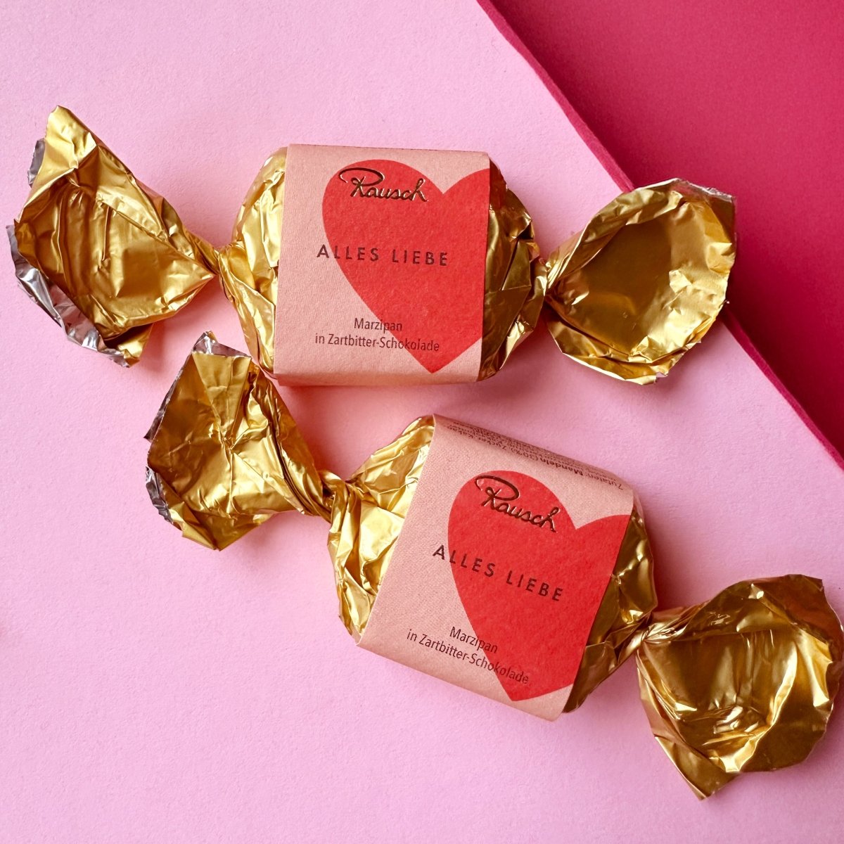 Rausch Alles Liebe Marzipan Happen in goldener Folie auf rosa Hintergrund.