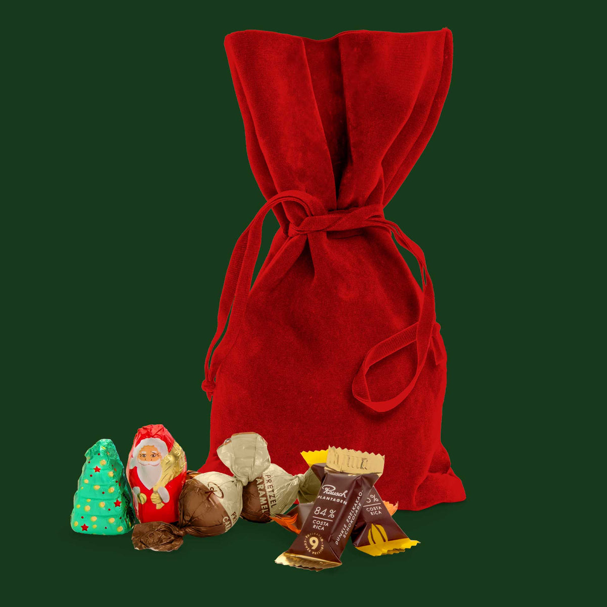 Rotes Samtsäckchen mit Pralinen, Schokoladenweihnachtsmann und Weihnachtsbaum vor grünem Hintergrund.