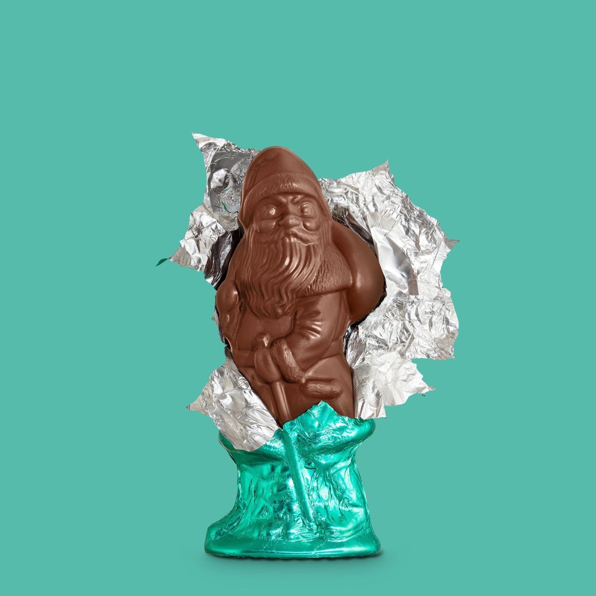 Schokoladen-Weihnachtsmann teils in grüner Folie verpackt, vor türkisfarbenem Hintergrund.