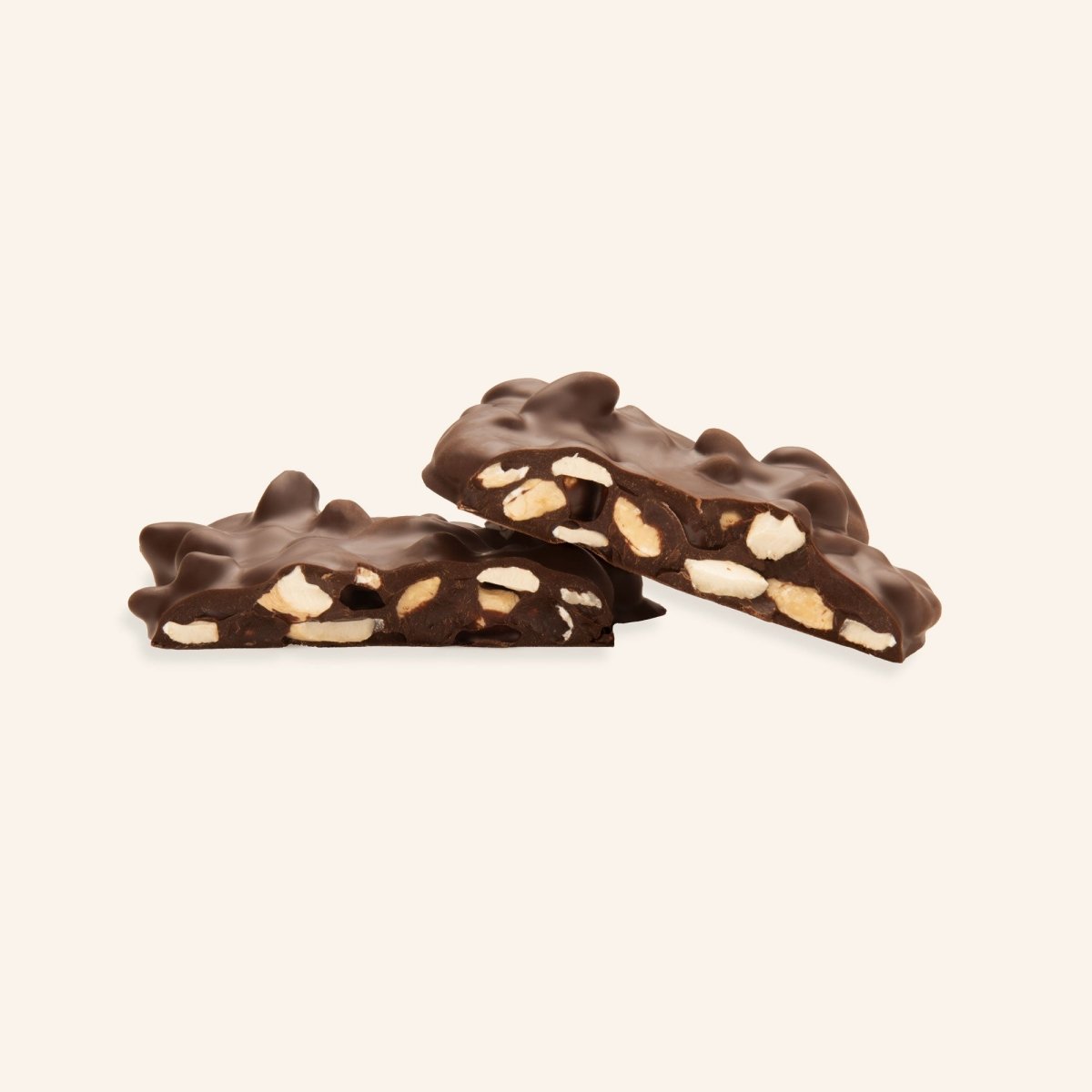 Dunkle Schokolade mit ganzen Cashewstücken, gebrochen in zwei Hälften auf cremefarbenem Hintergrund.