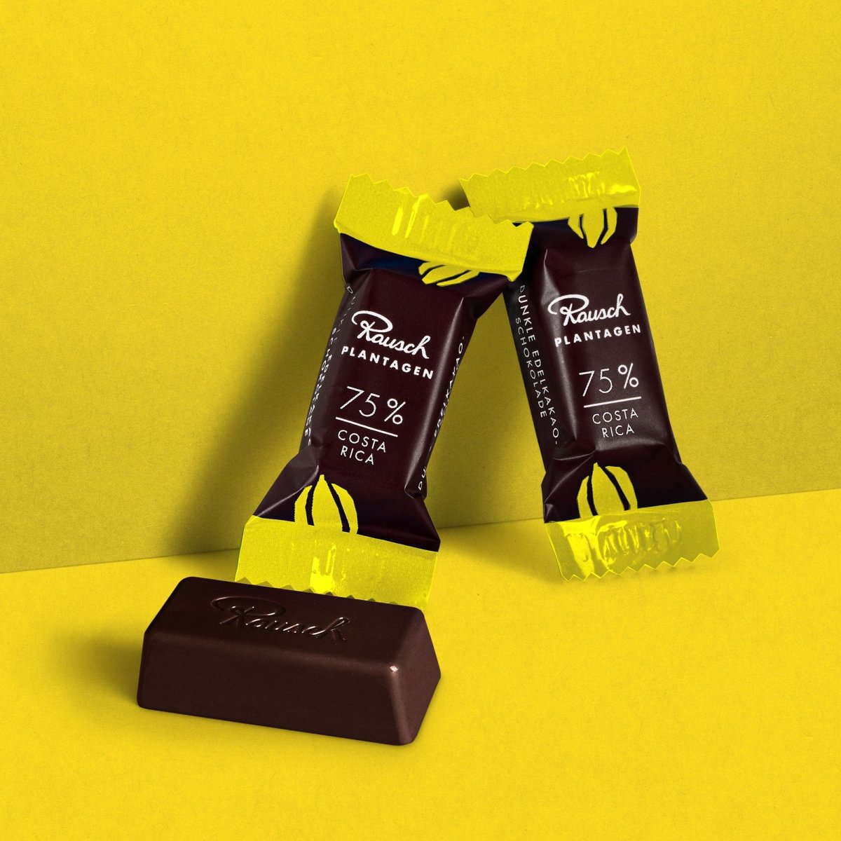 Rausch Costa Rica 75% Schokolade, zwei Pralinen in gelber Verpackung auf gelbem Hintergrund.