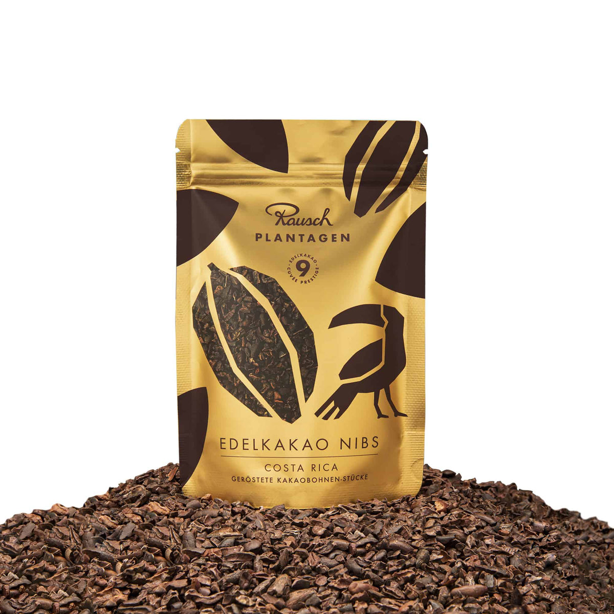 Rausch Edelkakao Nibs in goldener Verpackung auf einem Haufen gerösteter Kakaobohnenstücke, Costa Rica.