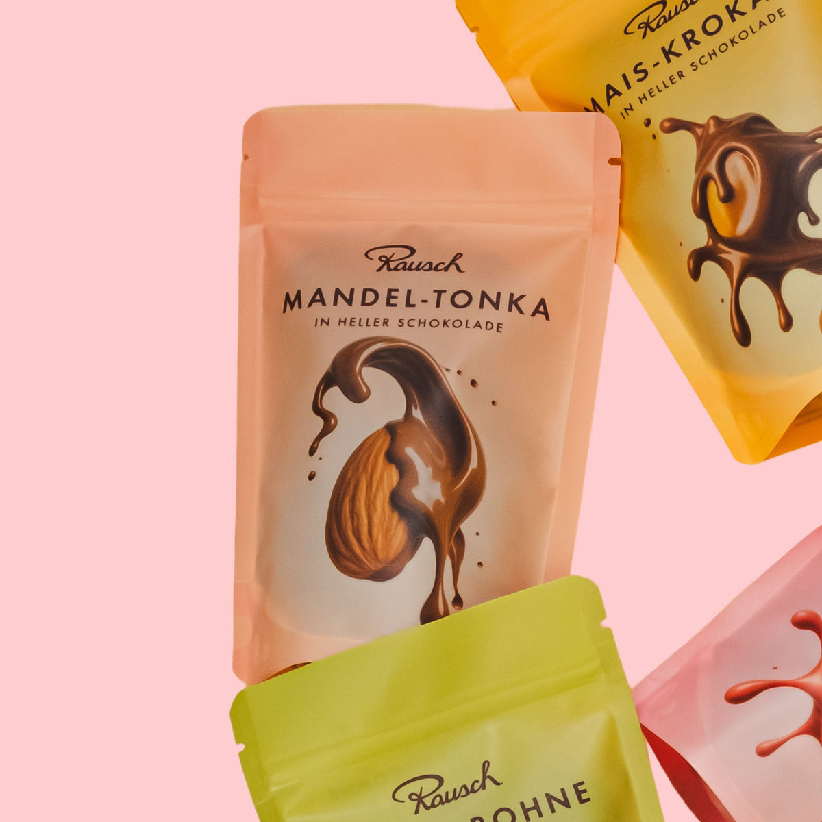 Verpackung "Mandel-Tonka" von Rausch, helle Schokolade, auf rosa Hintergrund, andere Sorten teils sichtbar.