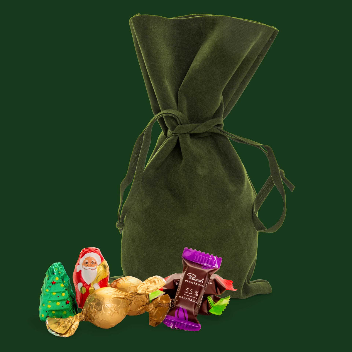 Grünes Samtsäckchen mit Schokolade, Weihnachtsmann, Tannenbaum und bunte Pralinen vor dunkelgrünem Hintergrund.