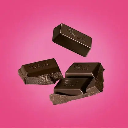 Dunkle Schokoladenstücke vor rosa Hintergrund, elegantes Design von Rausch Chocoladen.