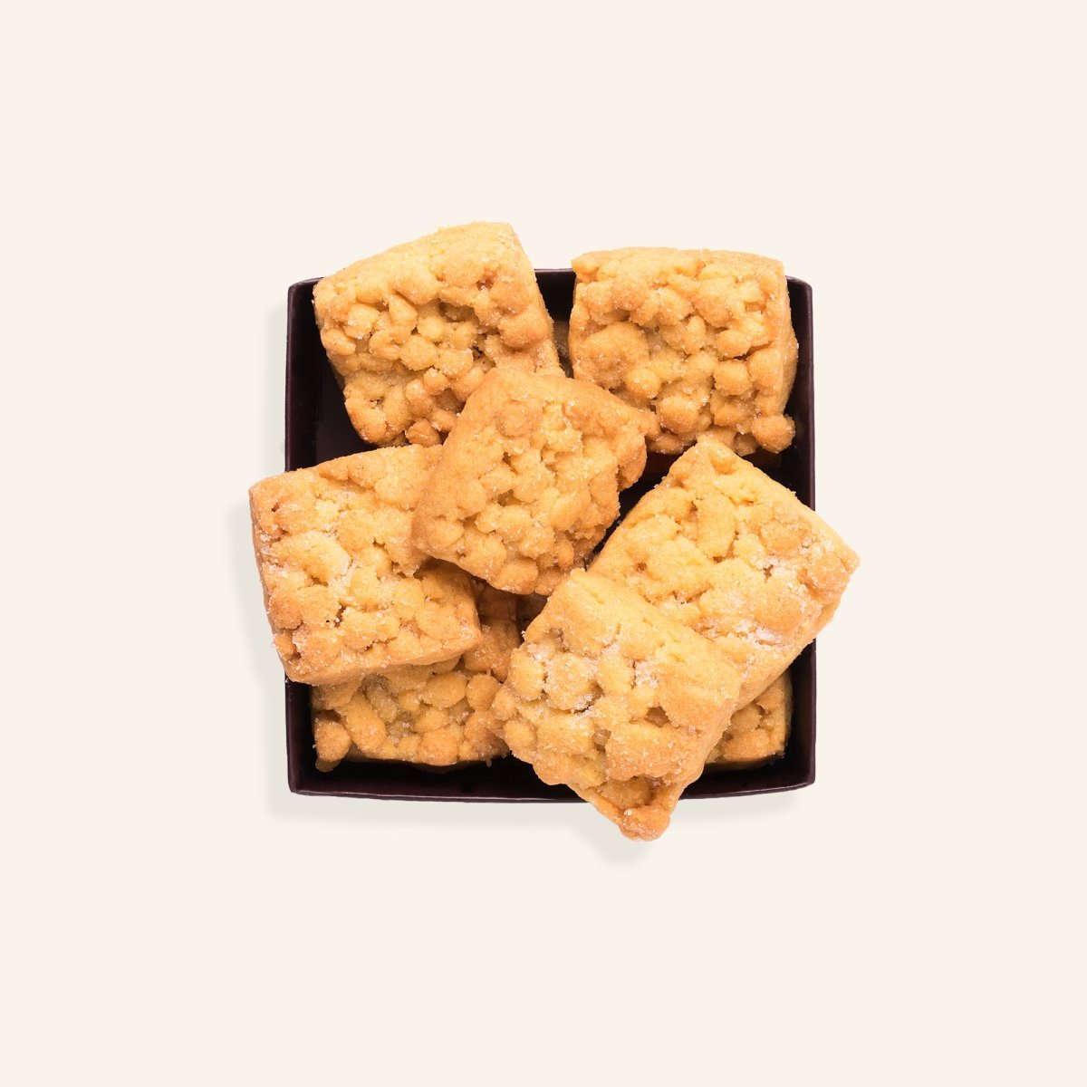 Sechs goldbraune Kekse mit Streuseln auf einer dunklen Schachtel.