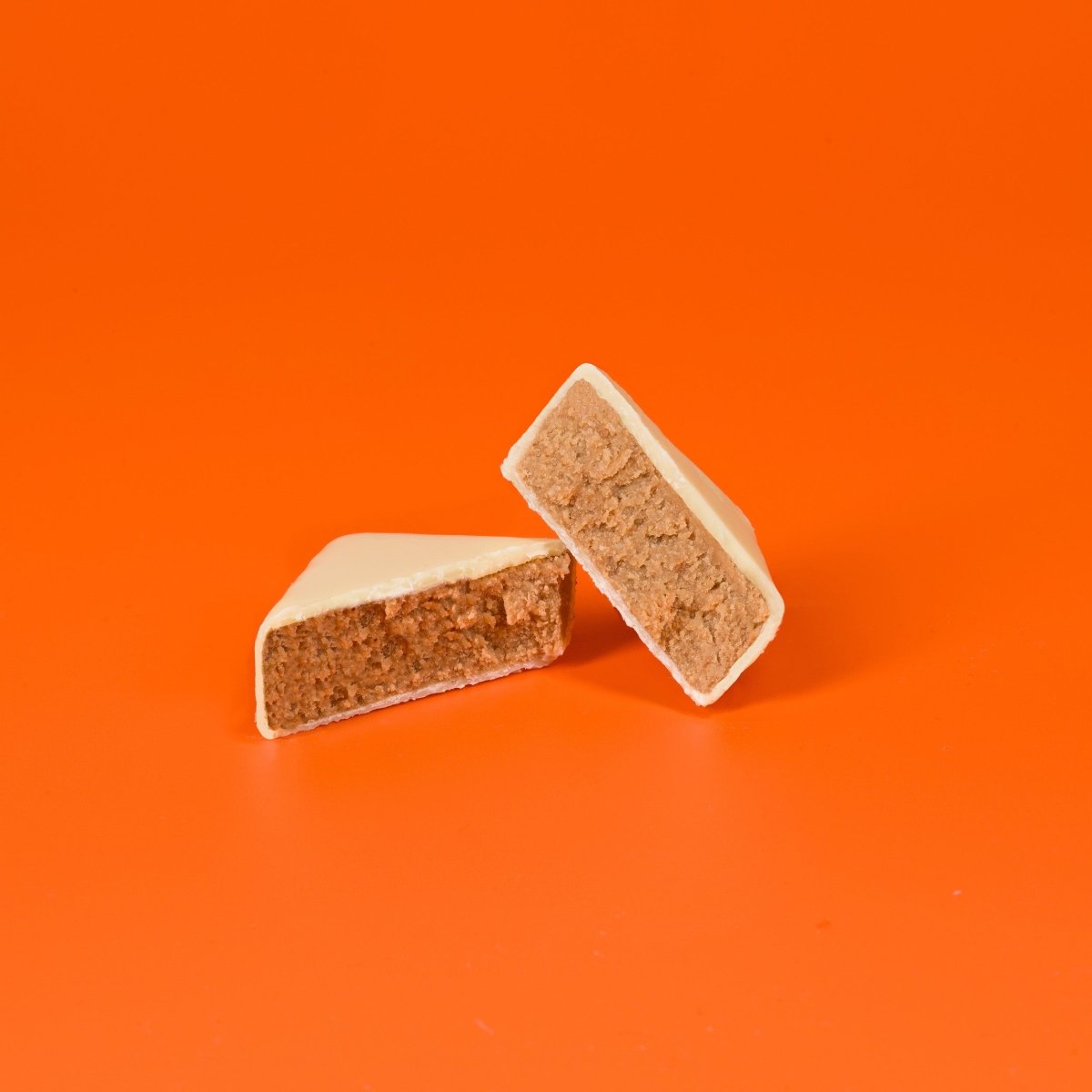 Weißer Schokoladenhappen mit Erdbeerfüllung, angeschnitten auf orangefarbenem Hintergrund.