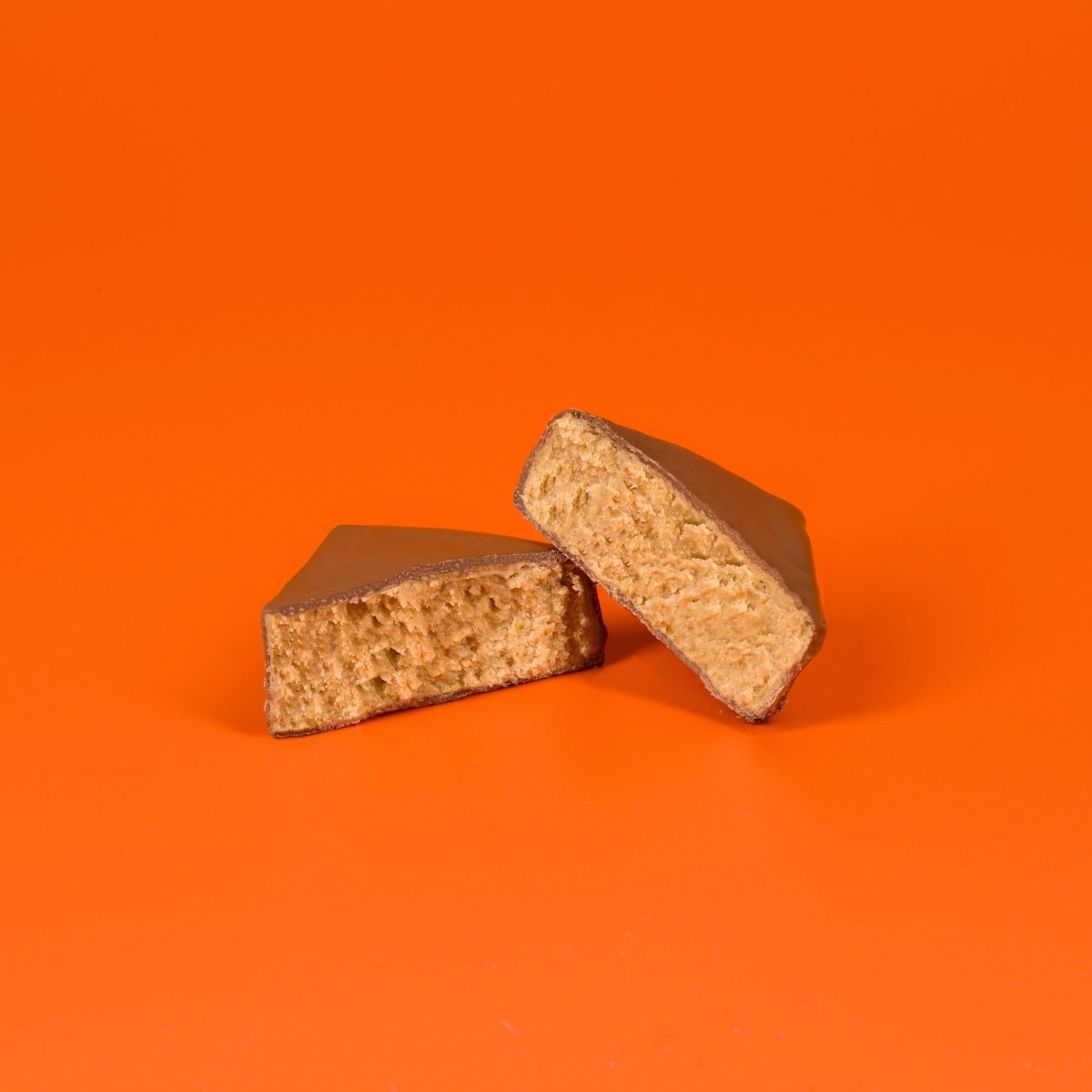 Aufgeschnittene Schokolade mit Marillenfüllung auf orangefarbenem Hintergrund.