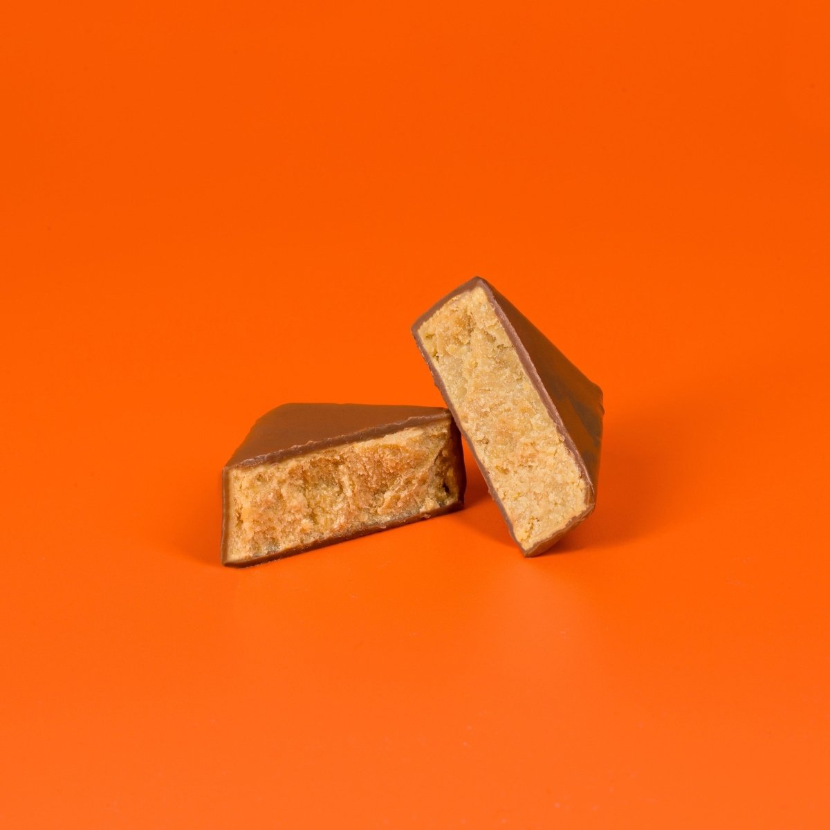 Aufgeschnittener Schokoladenhappen mit Sanddorn-Orange-Füllung auf orangem Hintergrund.