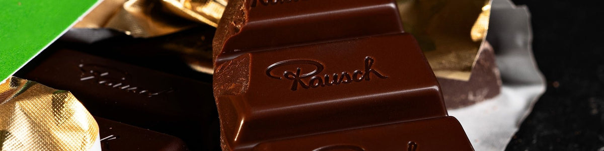Nahaufnahme von Rausch Schokolade, teils ausgepackt, mit eingeprägtem Markenlogo auf dunkler Schokolade.