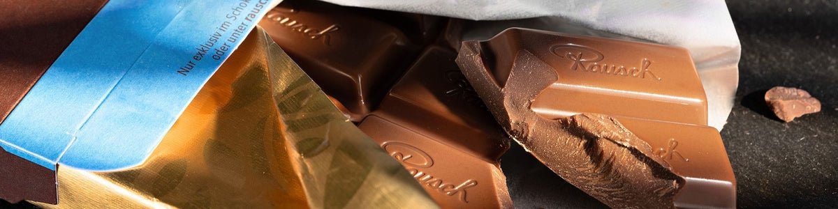 Nahaufnahme von geöffneten Schokoladentafeln mit Rausch-Prägung, teils in goldener Verpackung.