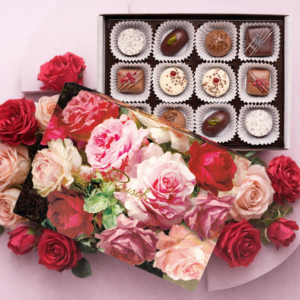 Pralinenbox mit Rosenmuster, umgeben von roten und rosafarbenen Rosenblüten.