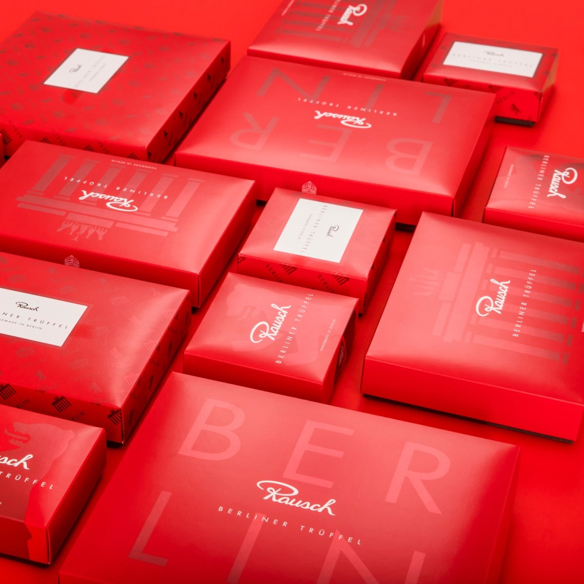 Rote Geschenkboxen von Rausch Berlin Trüffel auf rotem Hintergrund, elegant angeordnet.