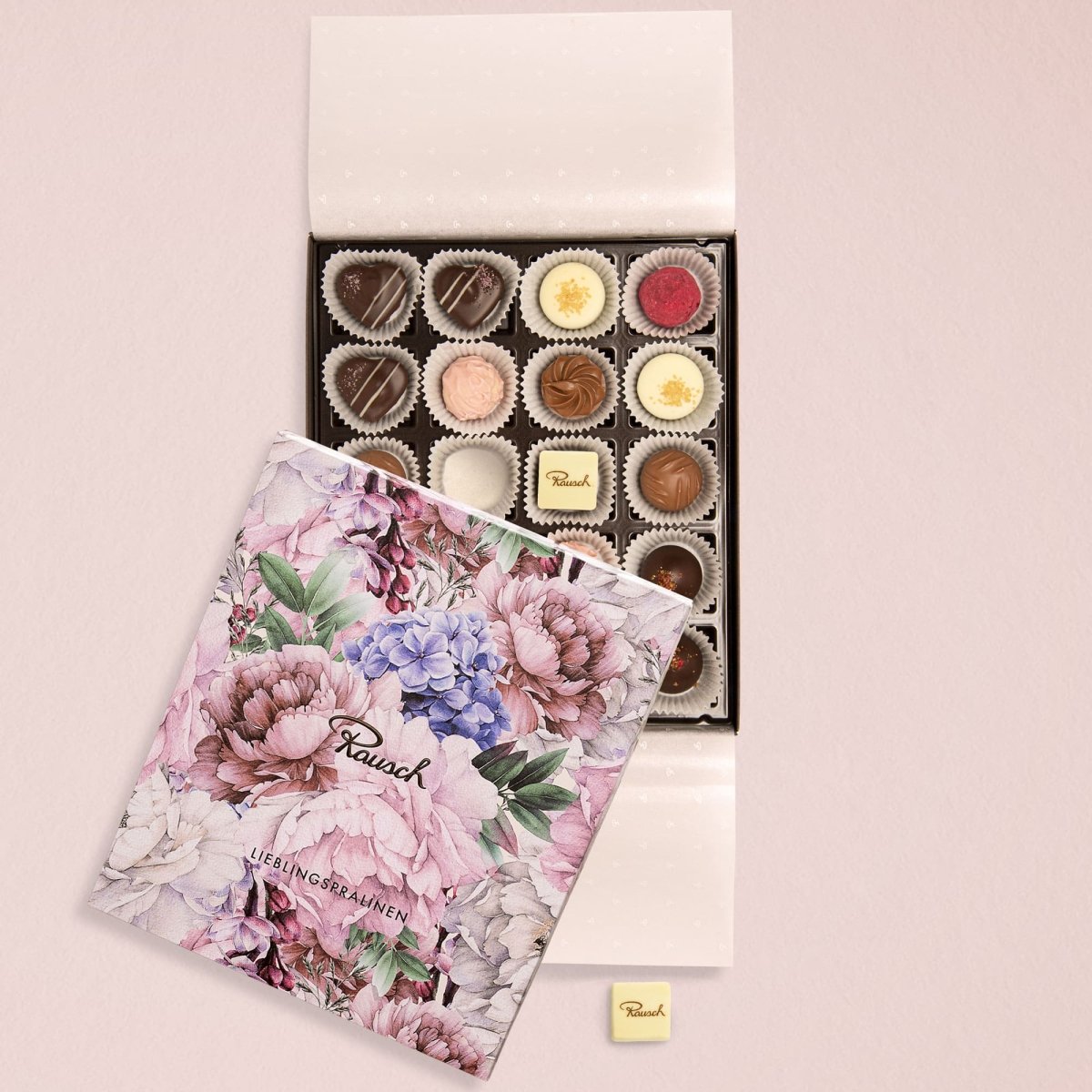 Offene Pralinenschachtel mit 20 Pralinen und floral verziertem Deckel auf hellem Hintergrund.