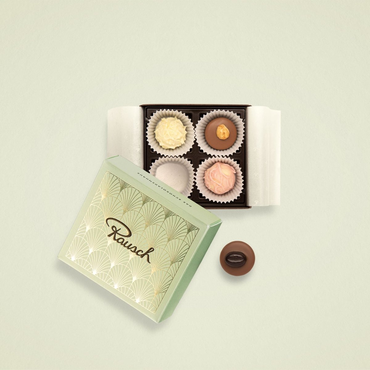Elegante Schachtel mit vier klassischen Pralinen auf hellgrünem Hintergrund.