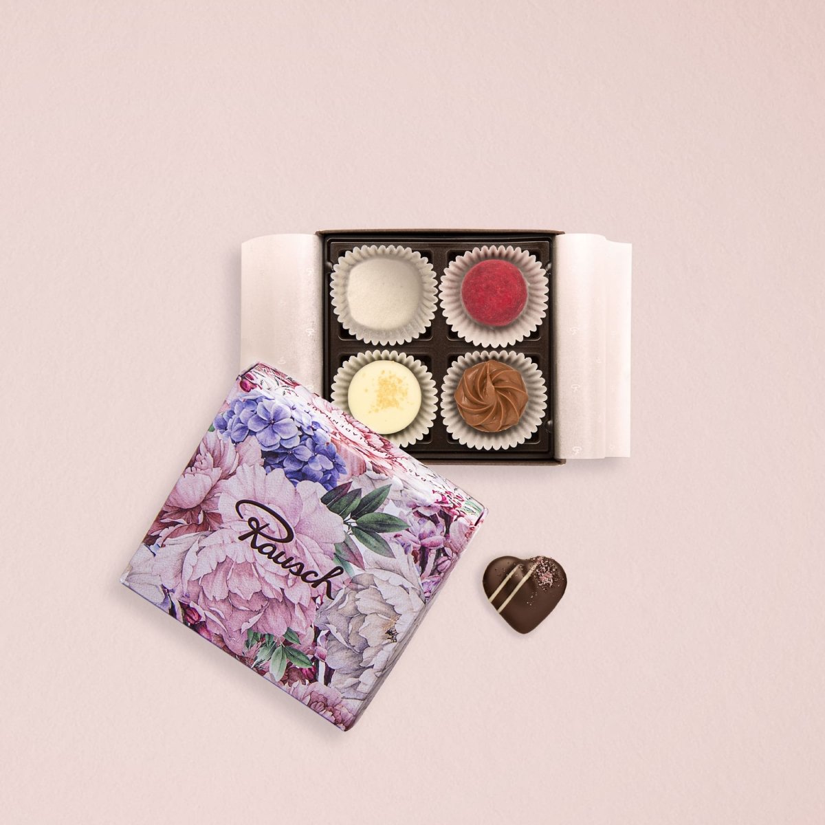 Pralinenverpackung mit vier Pralinen und floralem Design, daneben eine herzförmige Praline.