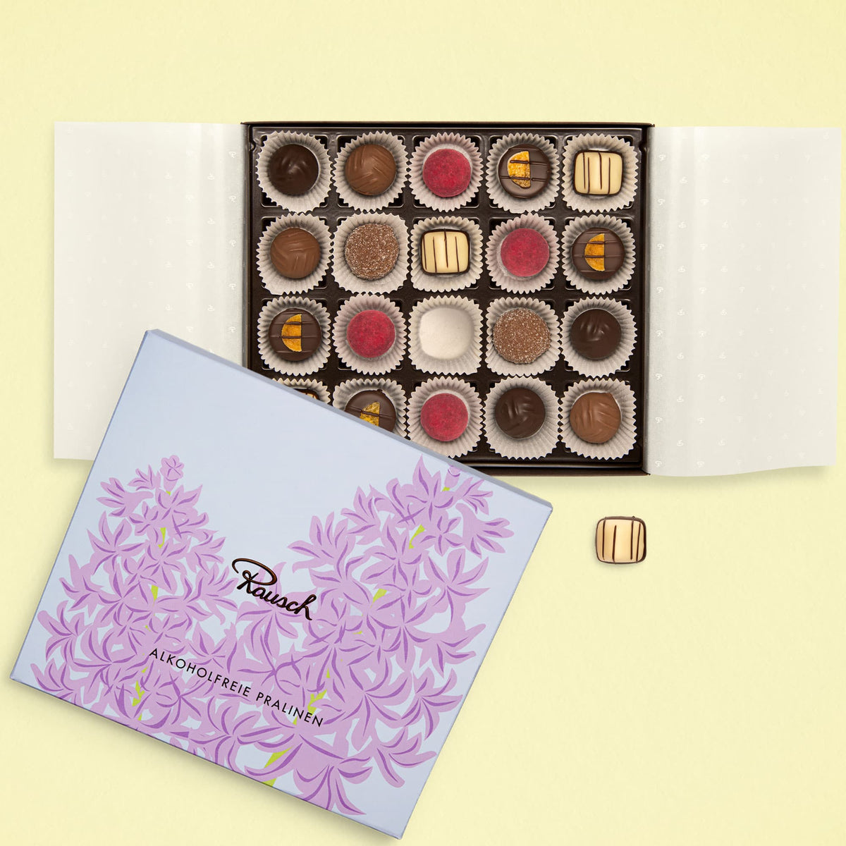 Offene Pralinenschachtel mit 20 alkoholfreien Pralinen von Rausch, dekorativer lila Verpackung im Osterdesign.