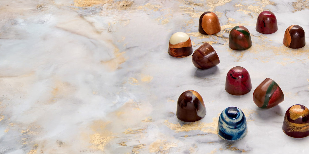 Bunte Pralinen auf einem marmorierten Untergrund, teils mit goldenen Verzierungen.