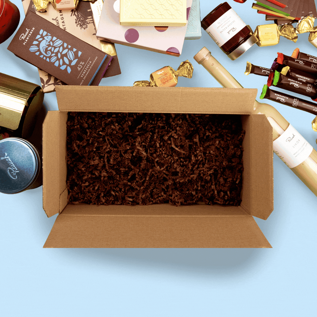 Offene Box mit Schokoladen, Pralinen und Geschenken auf blauem Hintergrund, umgeben von edlen Verpackungen.