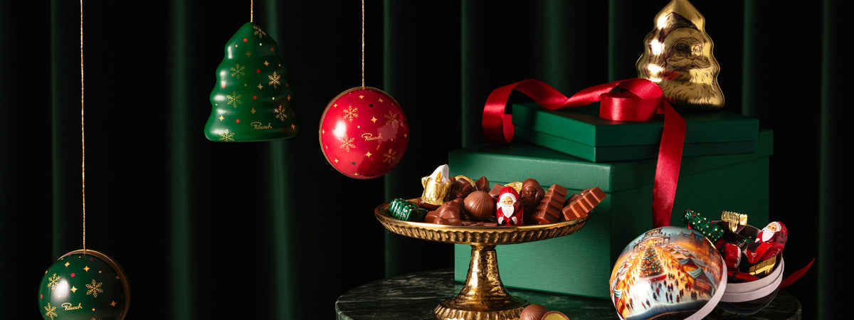 Weihnachtliche Pralinen und Dekorationen vor grünem Hintergrund: Schokolade in Formen und festliche Kugeln, rot-grünes Farbschema.