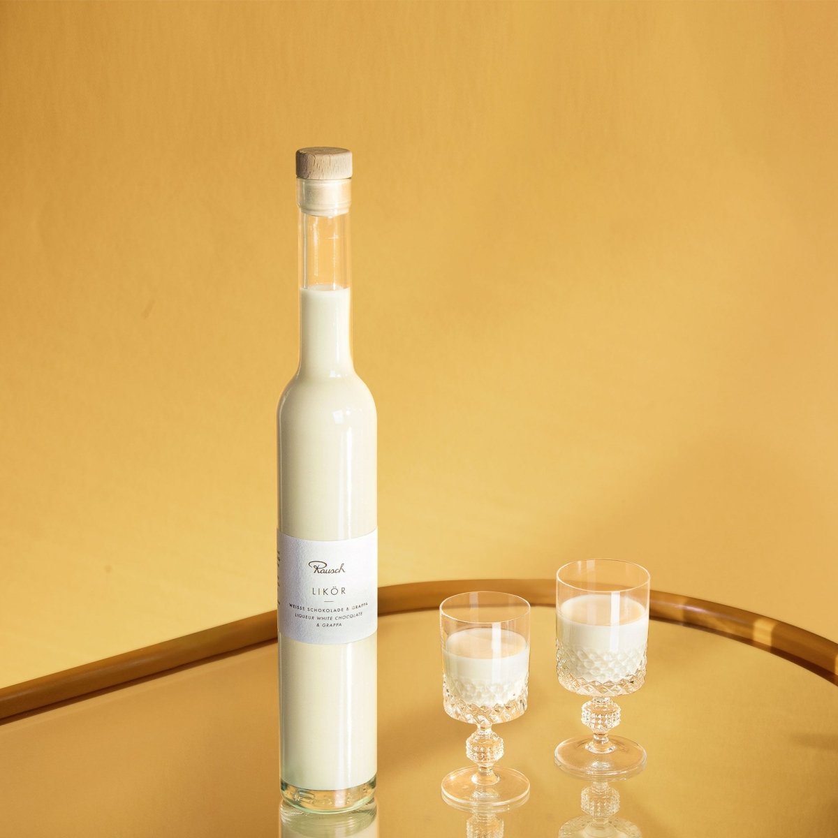 Flasche mit weißem Likör und zwei mit Likör gefüllte Gläser auf goldenem Tisch vor gelbem Hintergrund.