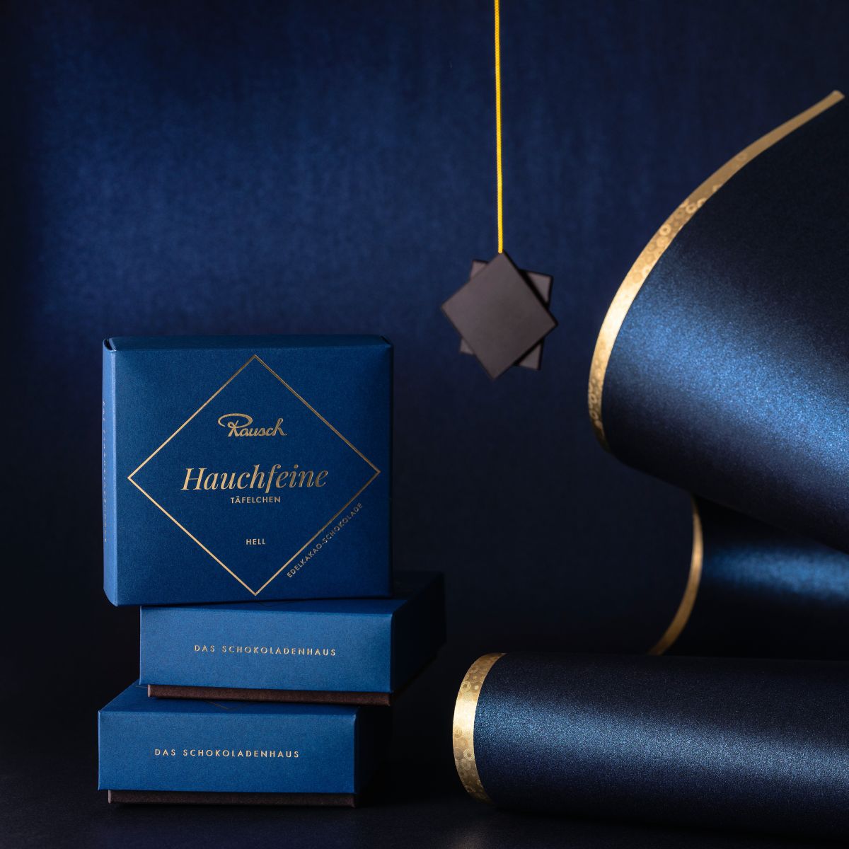 Elegante Rausch-Schokoladenverpackungen vor dunkelblauem Hintergrund mit goldenen Akzenten.