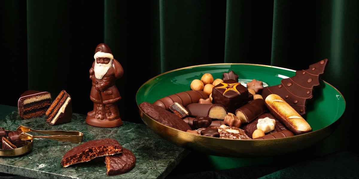 Verschiedene Pralinen und Schokoladen auf einem grünen Teller mit Schokoladen-Weihnachtsmann vor dunklem Hintergrund.